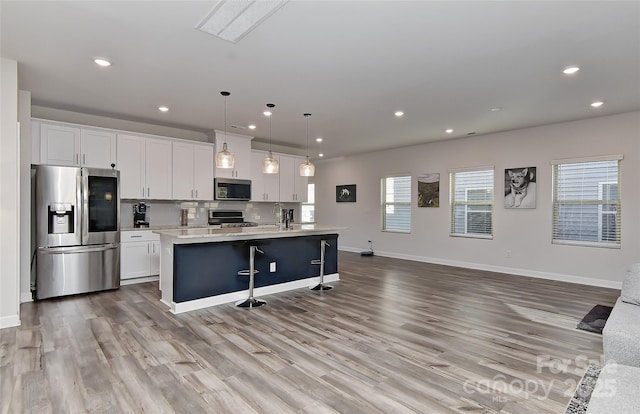 kitchen featuring a kitchen island with sink, a kitchen breakfast bar, appliances with stainless steel finishes, decorative light fixtures, and white cabinetry