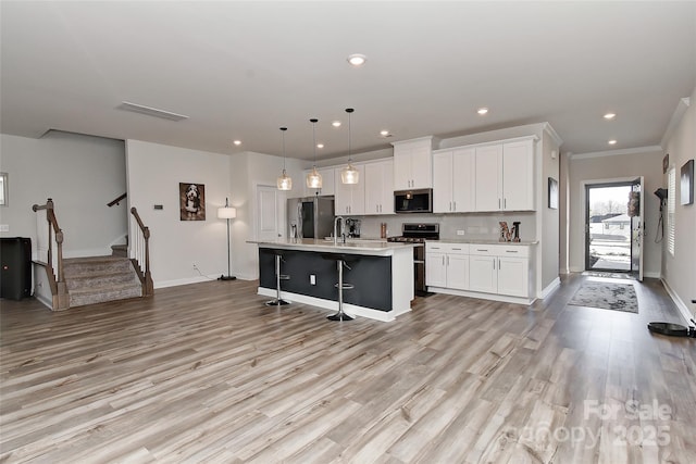 kitchen with a kitchen breakfast bar, stainless steel appliances, white cabinets, hanging light fixtures, and an island with sink