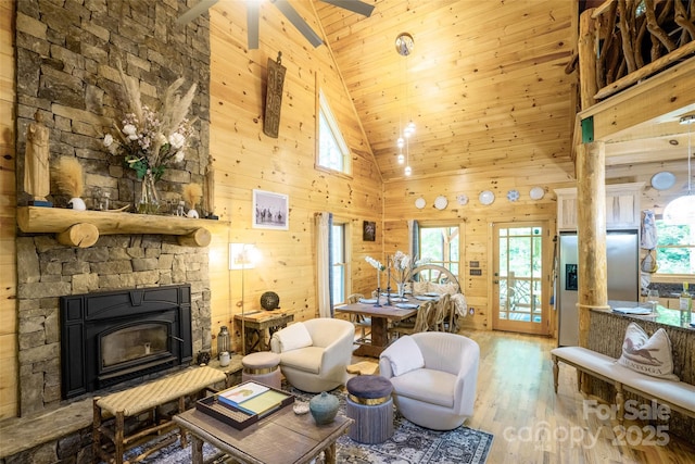 living room with ceiling fan, wood-type flooring, high vaulted ceiling, a fireplace, and wood walls