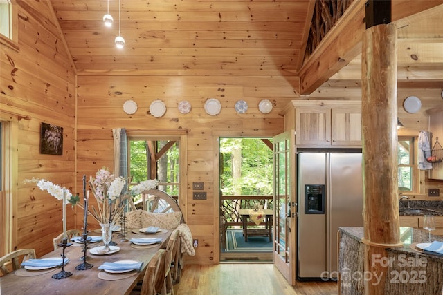 dining space featuring wooden walls, high vaulted ceiling, and light wood-type flooring