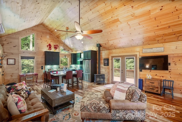 living room featuring light wood-type flooring, wood ceiling, high vaulted ceiling, a wood stove, and plenty of natural light