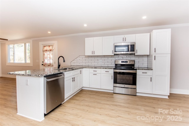 kitchen featuring sink, kitchen peninsula, stainless steel appliances, light stone countertops, and white cabinets