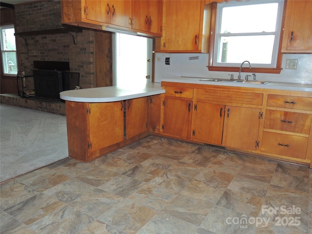 kitchen with kitchen peninsula, tasteful backsplash, light colored carpet, sink, and a fireplace