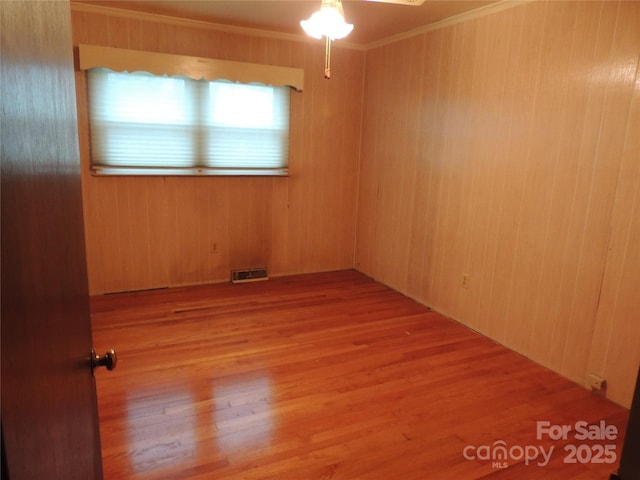 unfurnished room with wooden walls, light hardwood / wood-style floors, ceiling fan, and crown molding