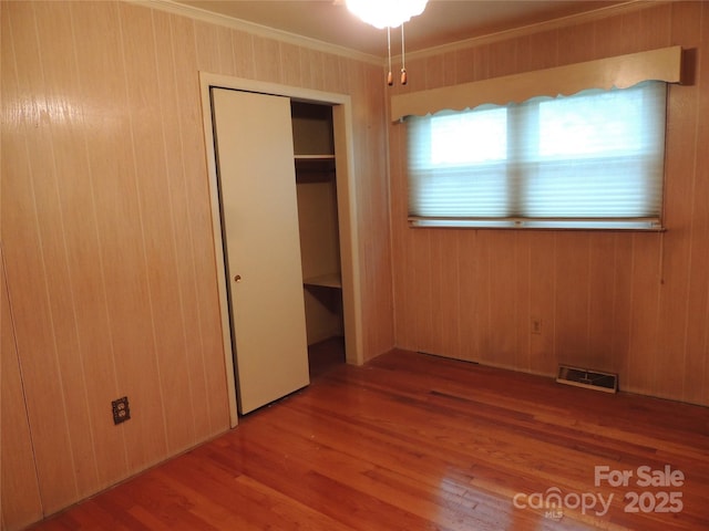 unfurnished bedroom with a closet, light hardwood / wood-style flooring, wood walls, and ornamental molding