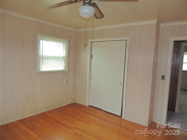 unfurnished bedroom with ceiling fan, crown molding, wood walls, light hardwood / wood-style floors, and a closet