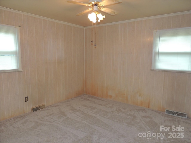 unfurnished room featuring light carpet, ceiling fan, crown molding, and wood walls