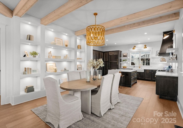 dining space with beamed ceiling, built in shelves, light hardwood / wood-style floors, and a notable chandelier