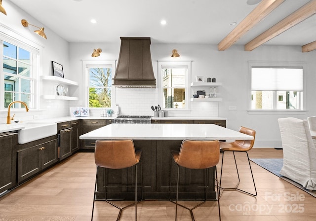 kitchen with custom exhaust hood, a breakfast bar, sink, beamed ceiling, and a kitchen island