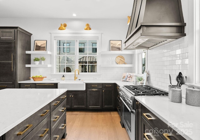 kitchen featuring light wood-type flooring, light stone counters, custom exhaust hood, high end stove, and sink