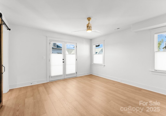 spare room featuring light wood-type flooring, french doors, a barn door, and ceiling fan