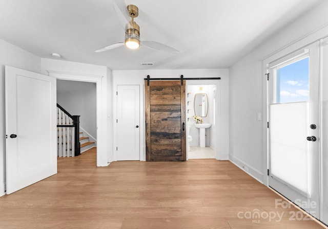 foyer entrance with light wood-type flooring, a barn door, and ceiling fan