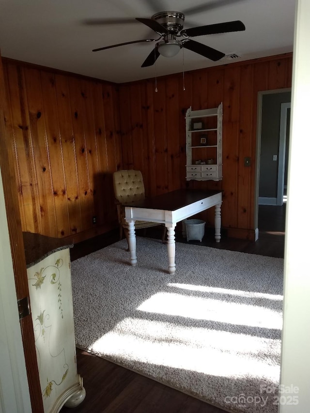 dining area featuring ceiling fan and wood walls