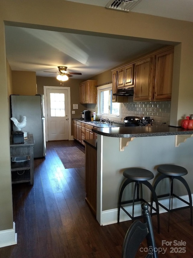 kitchen with stainless steel fridge, a kitchen bar, kitchen peninsula, and a wealth of natural light