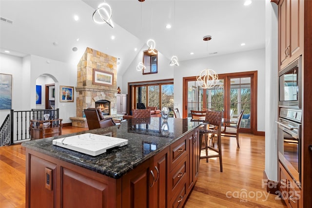 kitchen with a center island, dark stone counters, pendant lighting, a fireplace, and appliances with stainless steel finishes