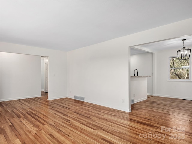 spare room with an inviting chandelier and light hardwood / wood-style flooring