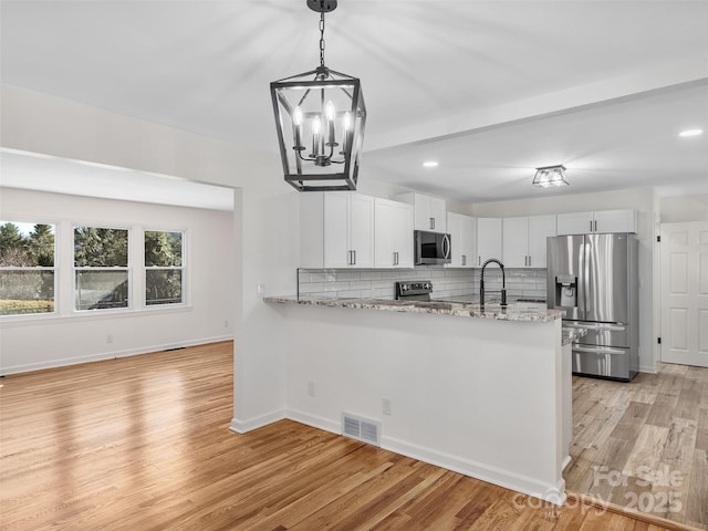 kitchen with white cabinetry, hanging light fixtures, stainless steel appliances, light stone counters, and kitchen peninsula