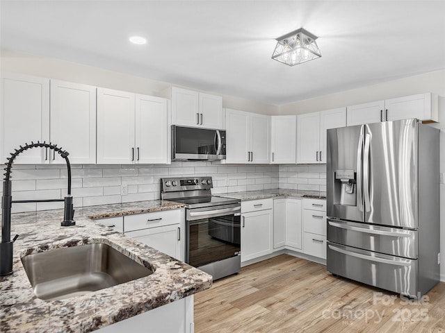 kitchen with white cabinets, sink, light hardwood / wood-style floors, light stone counters, and stainless steel appliances