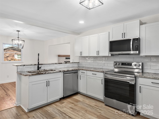 kitchen featuring kitchen peninsula, appliances with stainless steel finishes, tasteful backsplash, an inviting chandelier, and white cabinetry