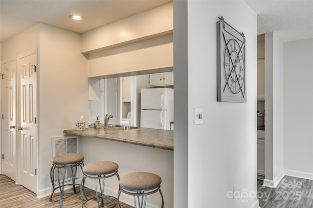 kitchen with white fridge, wood-type flooring, a kitchen breakfast bar, and sink