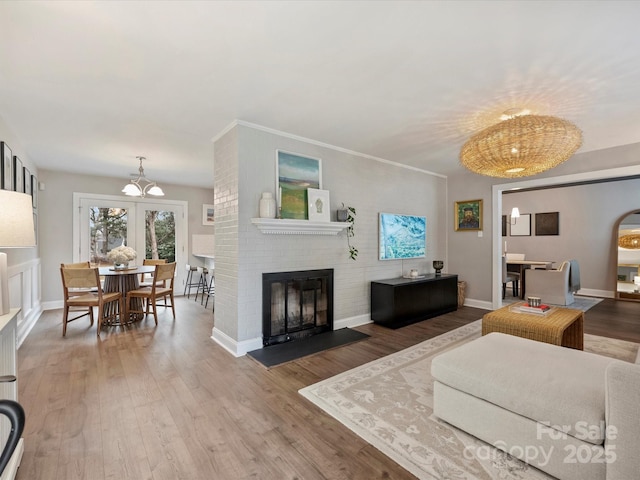 living room featuring ornamental molding, hardwood / wood-style floors, a brick fireplace, and a notable chandelier