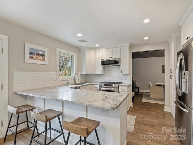 kitchen featuring white cabinetry, appliances with stainless steel finishes, a kitchen breakfast bar, and kitchen peninsula