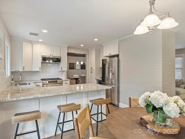 kitchen with sink, appliances with stainless steel finishes, hanging light fixtures, white cabinets, and kitchen peninsula