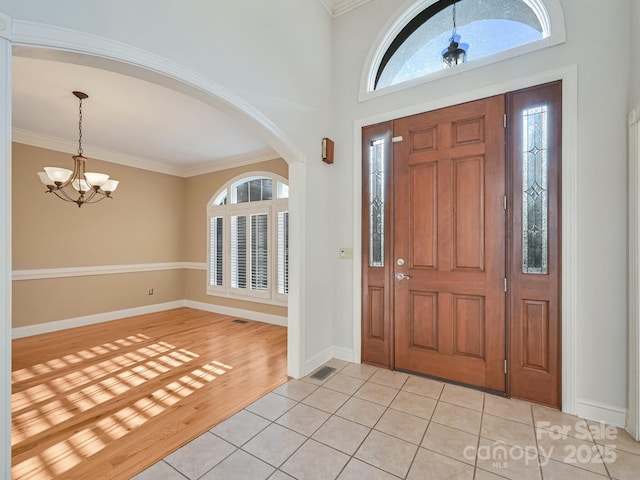 tiled entryway featuring ornamental molding and an inviting chandelier