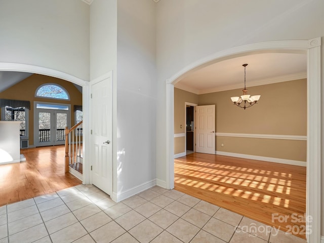 interior space with french doors, an inviting chandelier, crown molding, a towering ceiling, and light tile patterned floors