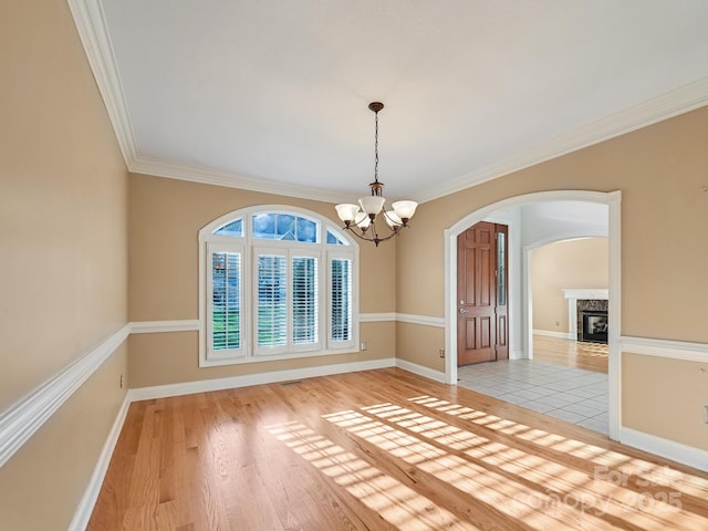 unfurnished dining area with a high end fireplace, a chandelier, light wood-type flooring, and ornamental molding