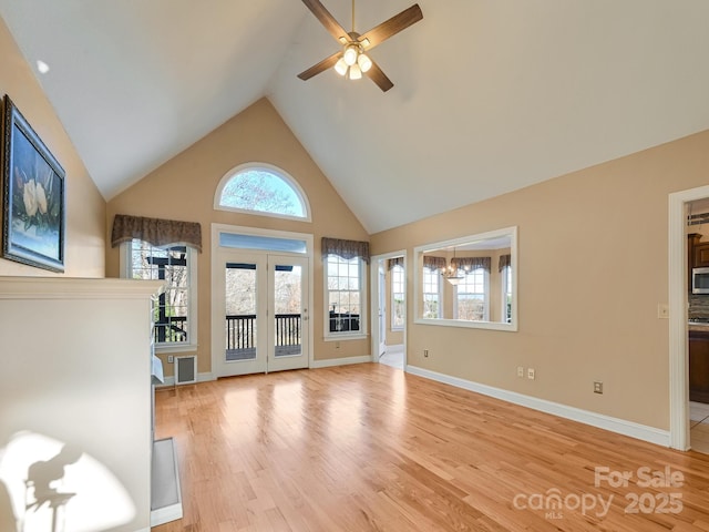 unfurnished living room with ceiling fan with notable chandelier, french doors, high vaulted ceiling, and light hardwood / wood-style flooring