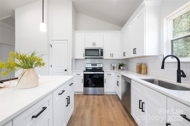 kitchen with sink, white cabinets, vaulted ceiling, and appliances with stainless steel finishes