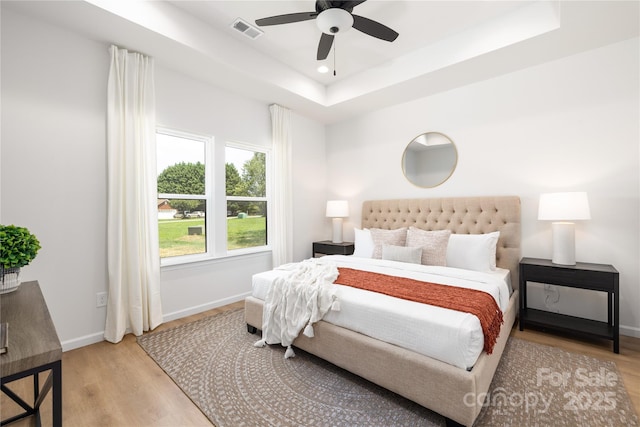 bedroom with ceiling fan, light hardwood / wood-style floors, and a raised ceiling