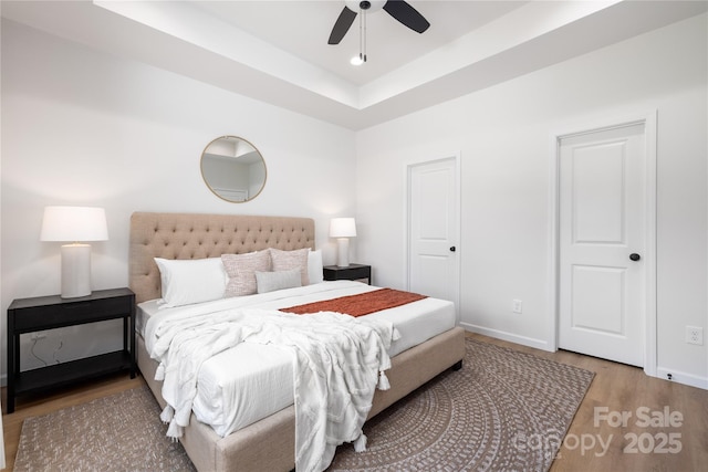 bedroom featuring hardwood / wood-style flooring, ceiling fan, and a raised ceiling