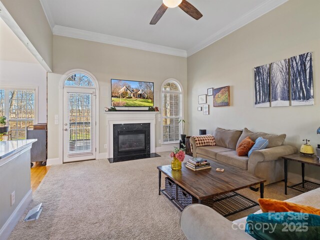 carpeted living area with visible vents, ornamental molding, a high end fireplace, a ceiling fan, and baseboards