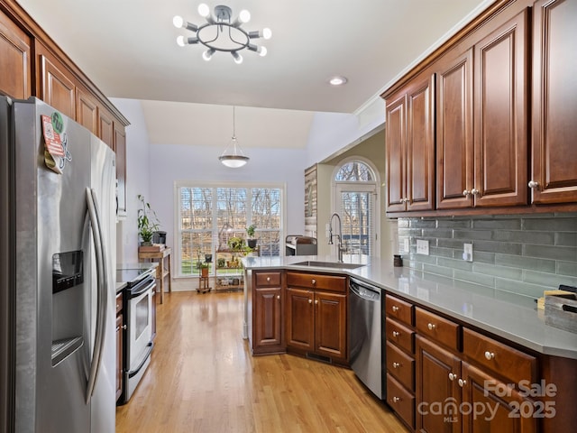 kitchen featuring light wood-style flooring, a peninsula, a sink, appliances with stainless steel finishes, and tasteful backsplash