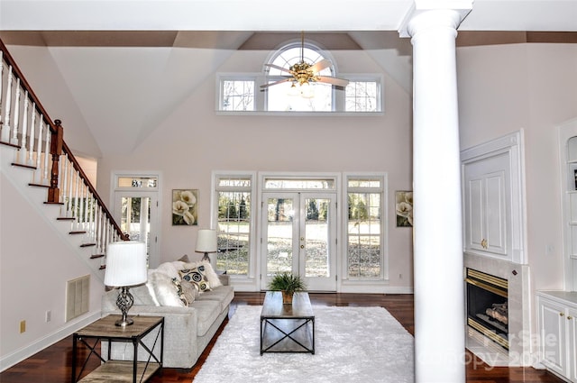 living room featuring a tile fireplace, ornate columns, ceiling fan, french doors, and a high ceiling