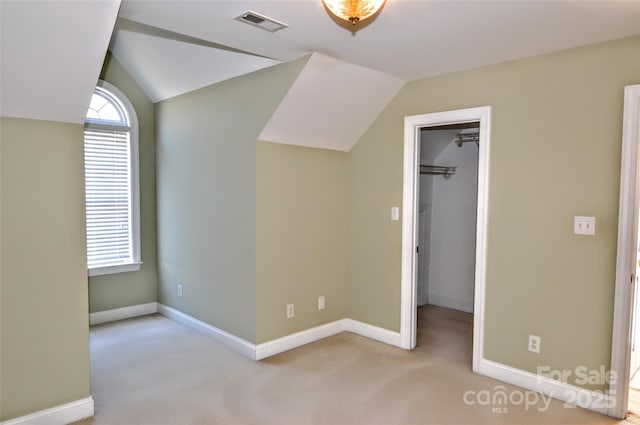 unfurnished bedroom with a walk in closet, vaulted ceiling, and light carpet