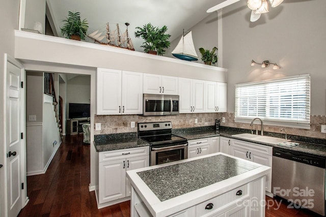 kitchen featuring stainless steel appliances, sink, high vaulted ceiling, a center island, and white cabinetry