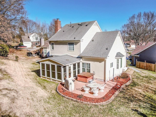 rear view of property featuring a lawn, a sunroom, a patio, and a hot tub