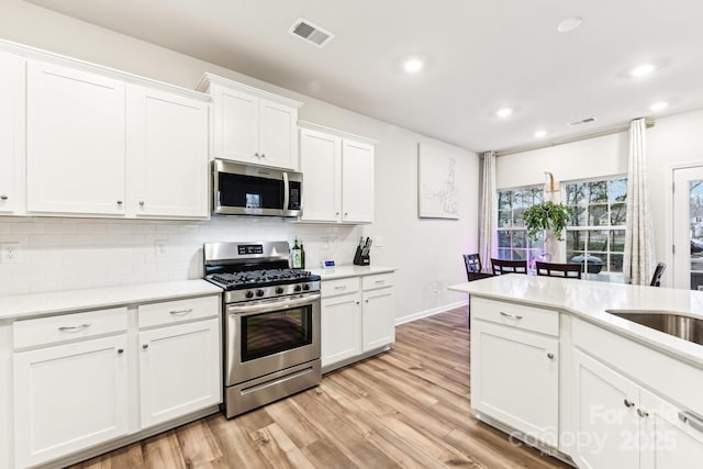 kitchen with sink, stainless steel appliances, backsplash, white cabinets, and light wood-type flooring