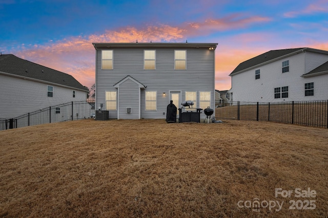 back house at dusk featuring a yard and central AC