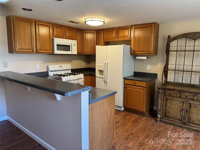 kitchen with kitchen peninsula, dark wood-type flooring, white appliances, and a kitchen bar