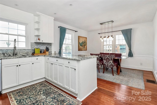 kitchen with sink, hanging light fixtures, kitchen peninsula, hardwood / wood-style floors, and white cabinets