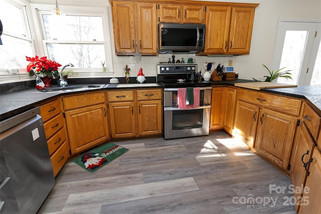 kitchen featuring hanging light fixtures, sink, light wood-type flooring, appliances with stainless steel finishes, and tasteful backsplash