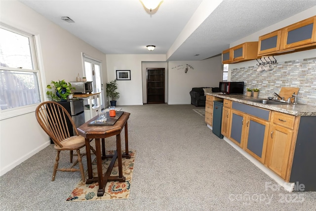 kitchen with light stone countertops, decorative backsplash, sink, and light colored carpet