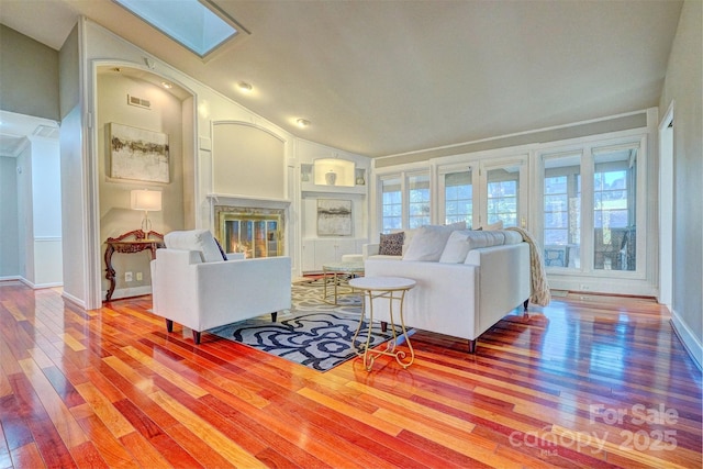 living room featuring hardwood / wood-style flooring, built in features, and a skylight