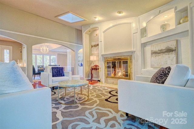 living room featuring a high end fireplace, built in shelves, an inviting chandelier, and hardwood / wood-style floors