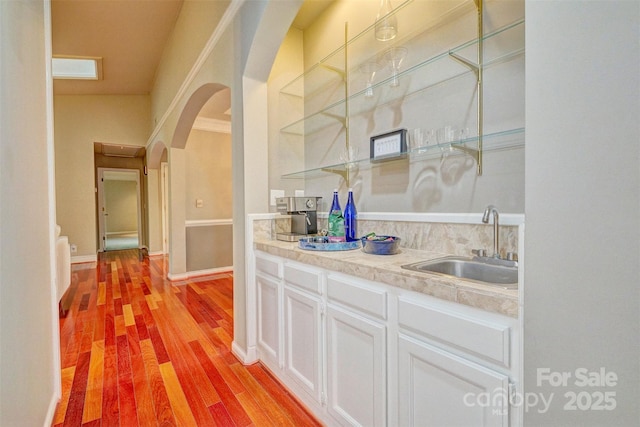 bar with white cabinetry, sink, and light hardwood / wood-style flooring