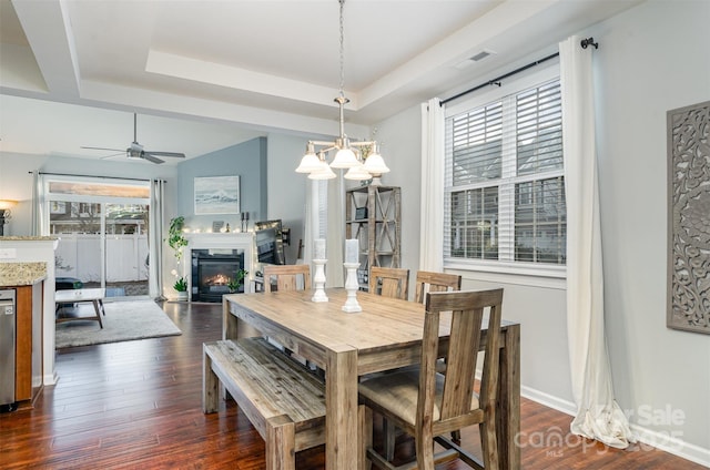 dining space with ceiling fan, a tray ceiling, and dark hardwood / wood-style flooring